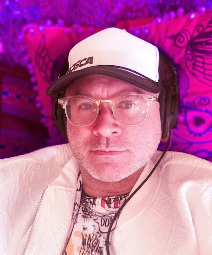 Erik O’Banion in a cap and headphones, lit in pink and purple.