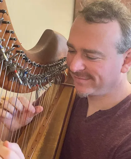Noah Brenner smiling as he plays a lever harp.
