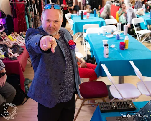 Rob Montango in a plaid jacket with a rose boutonnière, pointing at the camera.